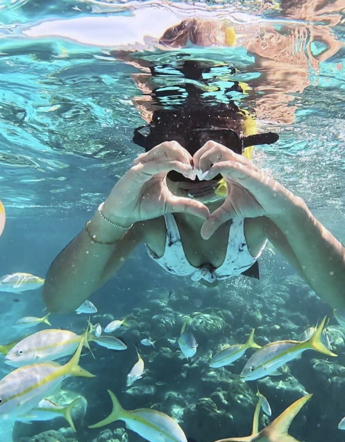 Snorkeler making heart with hands above reef fish at Icacos Island